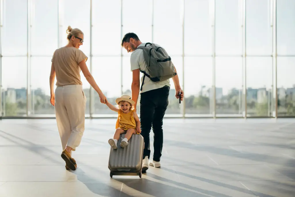 Family enjoying travel at airport terminal with child sitting on rolling luggage