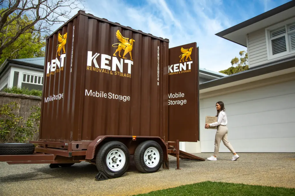 Woman carrying moving box toward Kent Removals & Storage mobile storage container in residential driveway