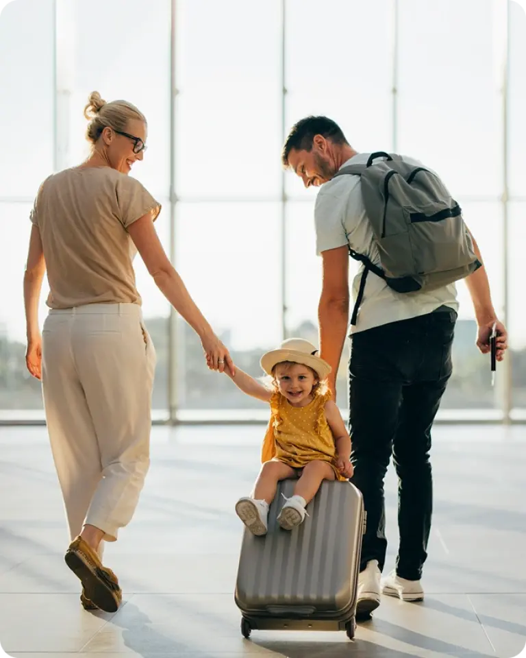Family enjoying travel at airport terminal with child sitting on rolling luggage