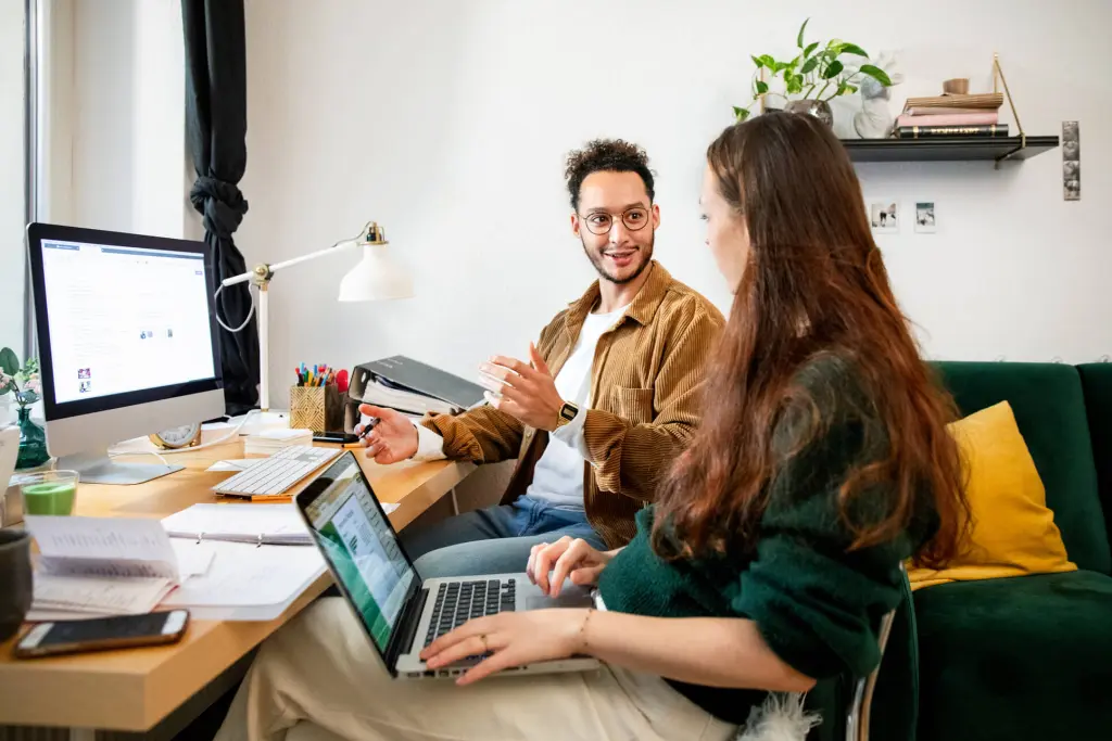 Two people discussing work at a desk with computers