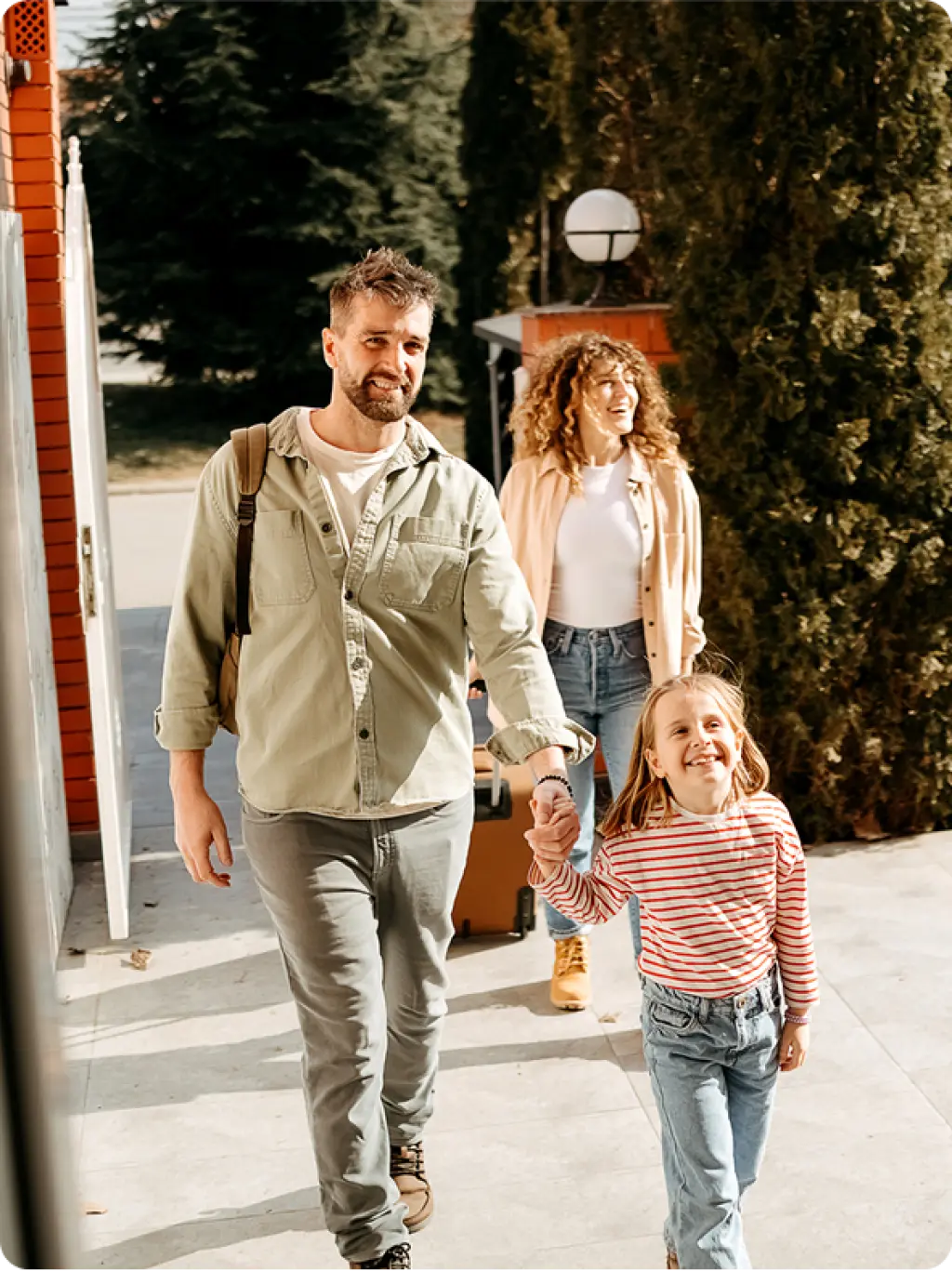 Smiling family of three walking together outdoors with luggage