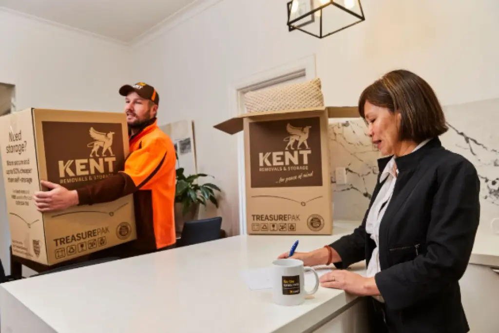 Kent Removals staff carrying TreasurePak box while customer signs paperwork in kitchen
