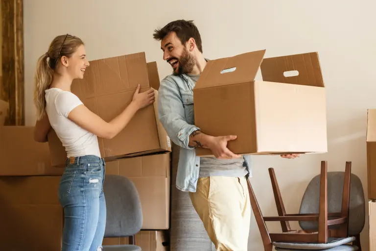 Couple carrying moving boxes together inside new home during relocation