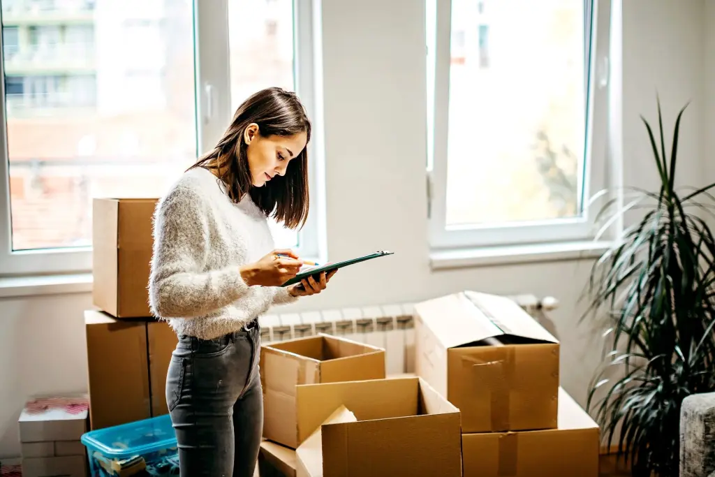 Woman checking moving checklist while packing boxes in new home