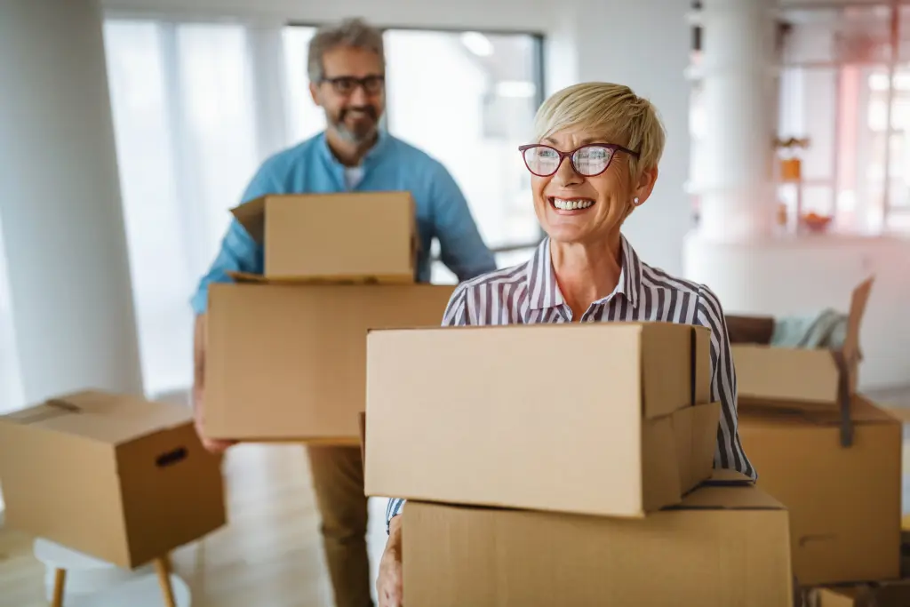 Senior couple carrying moving boxes inside their new home