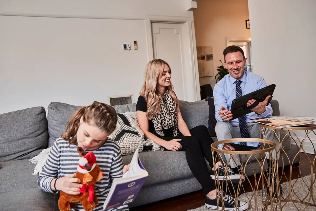 Family relaxing on sofa at home with parents looking at tablet and child reading