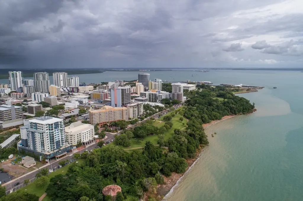 Aerial view of Darwin waterfront with city buildings, green parkland, and coastline under cloudy skies