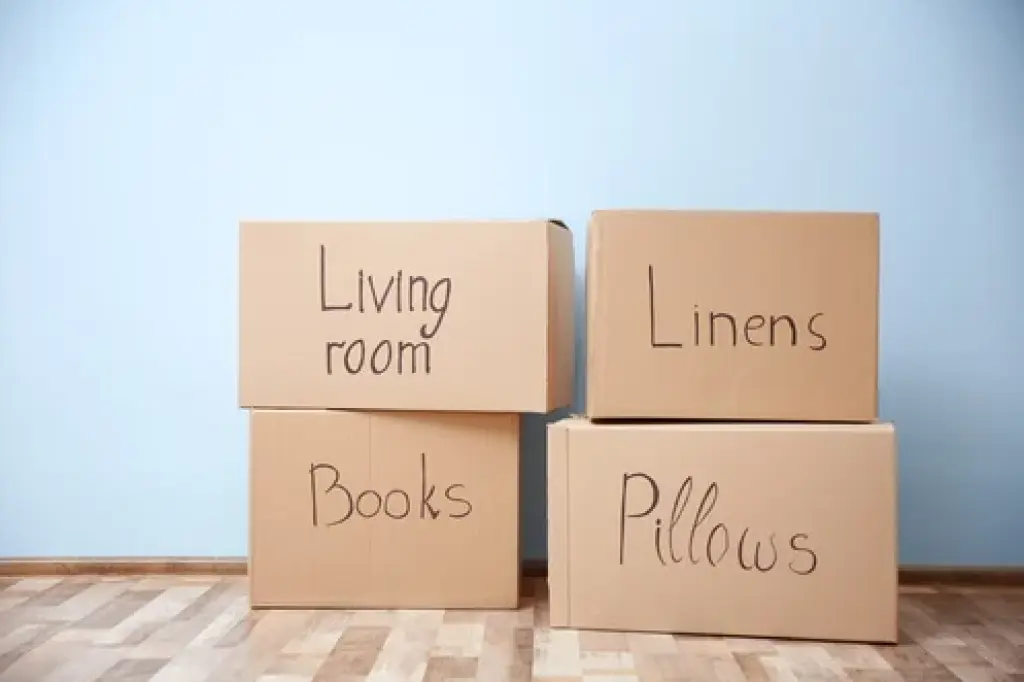 Four labeled moving boxes stacked against a wall reading Living Room, Linens, Books, and Pillows