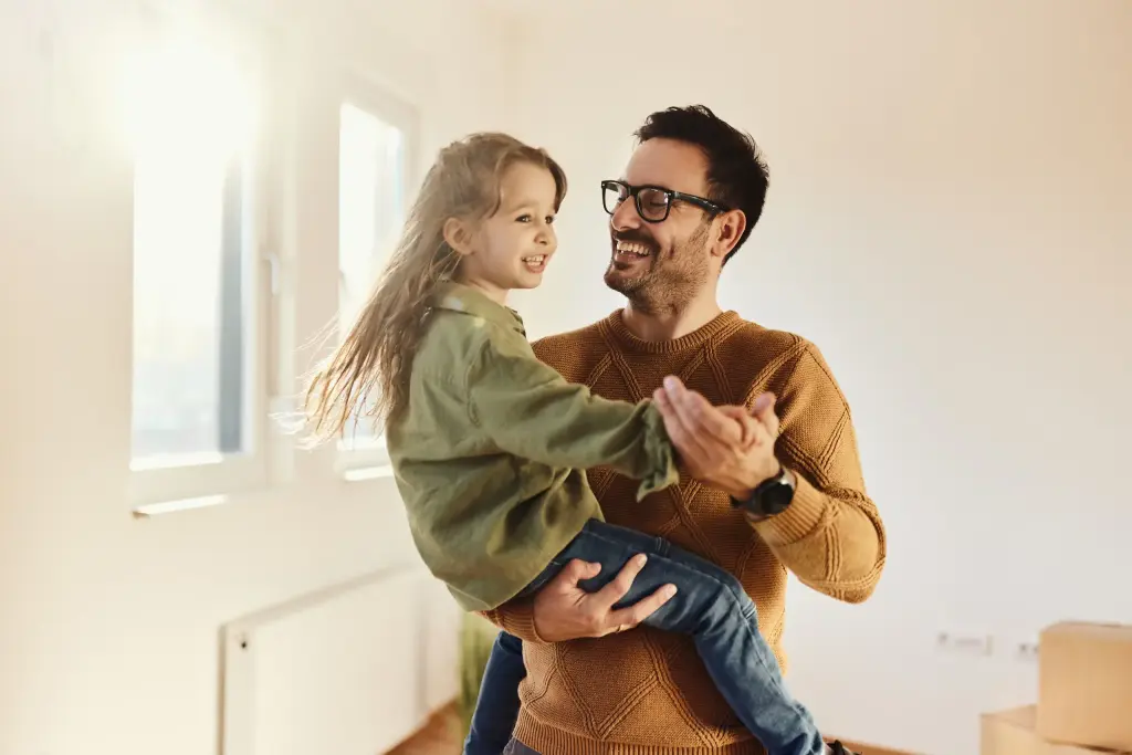 Happy father lifting and playing with daughter in empty room during house move